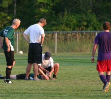 Two people assist an injured soccer player lying on the field while two other players stand nearby, highlighting the importance of Physical Therapy in Medford, NY for athletes’ recovery and care