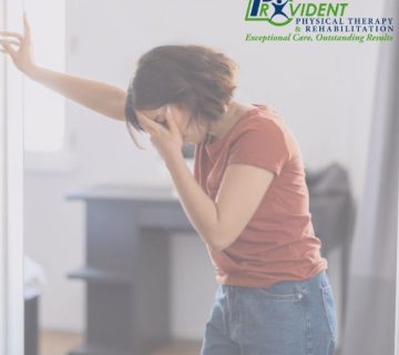 Woman standing indoors, leaning against a wall with one hand and covering her face with the other, appearing to experience discomfort from balance disorders; Provident Physical Therapy & Rehabilitation logo in the corner 